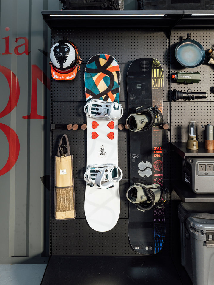 A snowboard, helmets and accessories displayed on a black PegGrid storage wall.