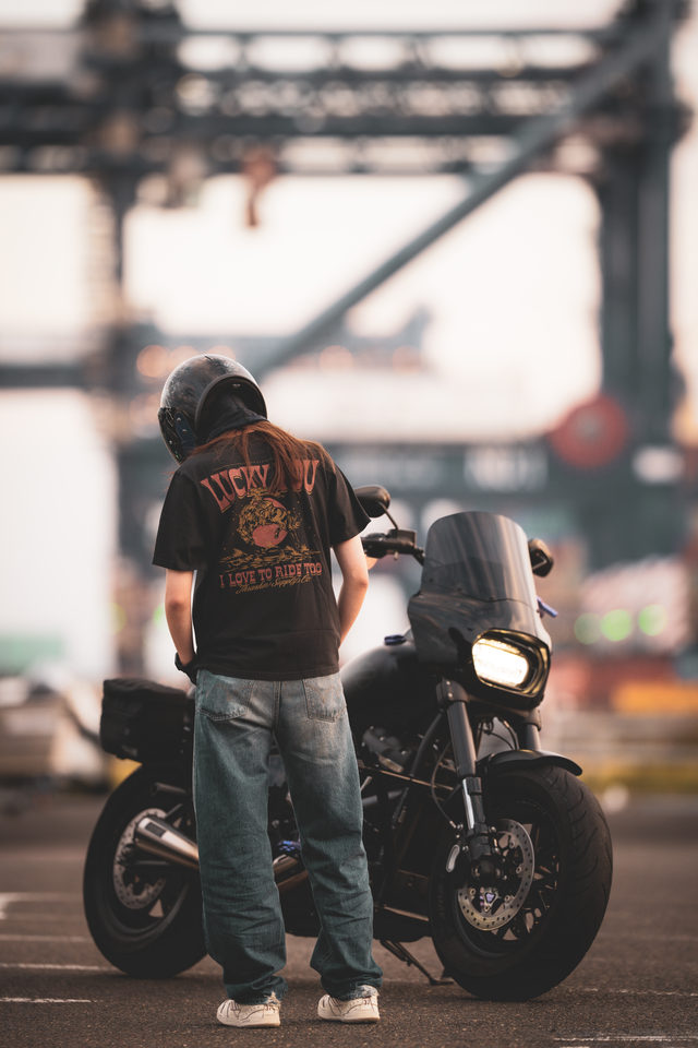 A rider standing beside a black motorcycle beneath an urban structure