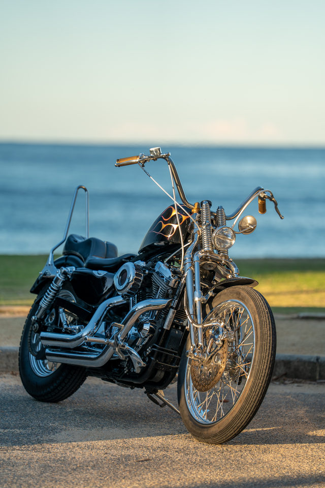 A custom motorcycle with a chrome front wheel parked beside the sea