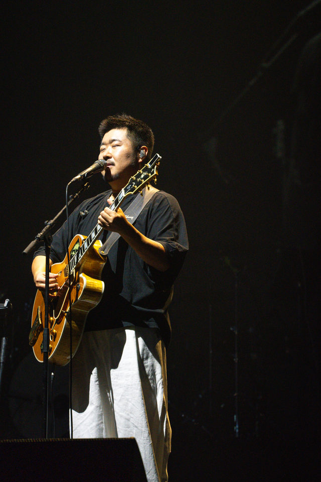A performer singing into a microphone while playing an acoustic guitar