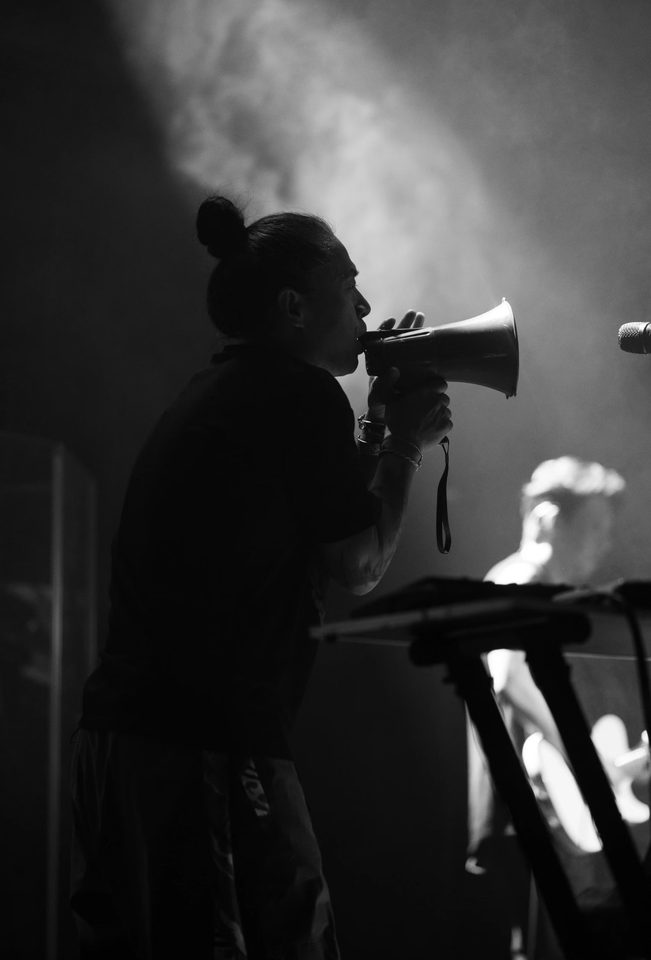 A black-and-white silhouette of a performer singing through a megaphone on stage